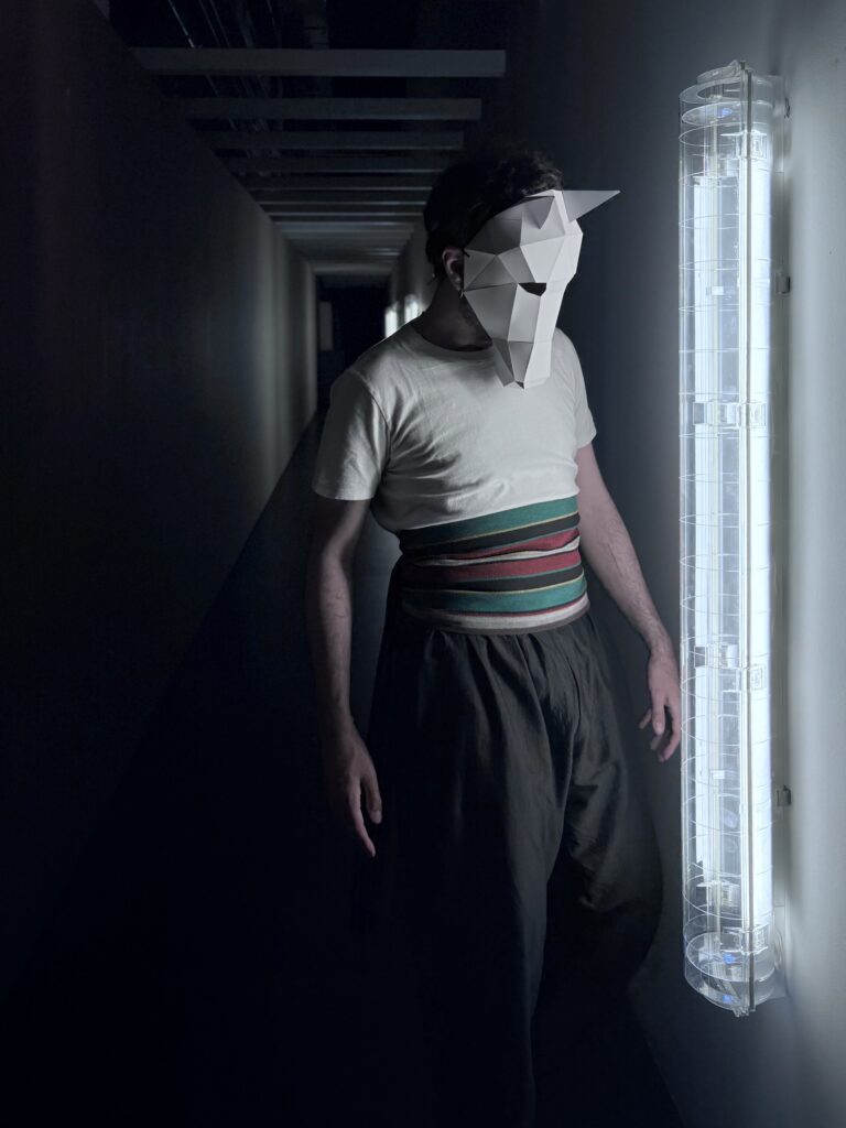 Persona con máscara geométrica en pasillo oscuro.