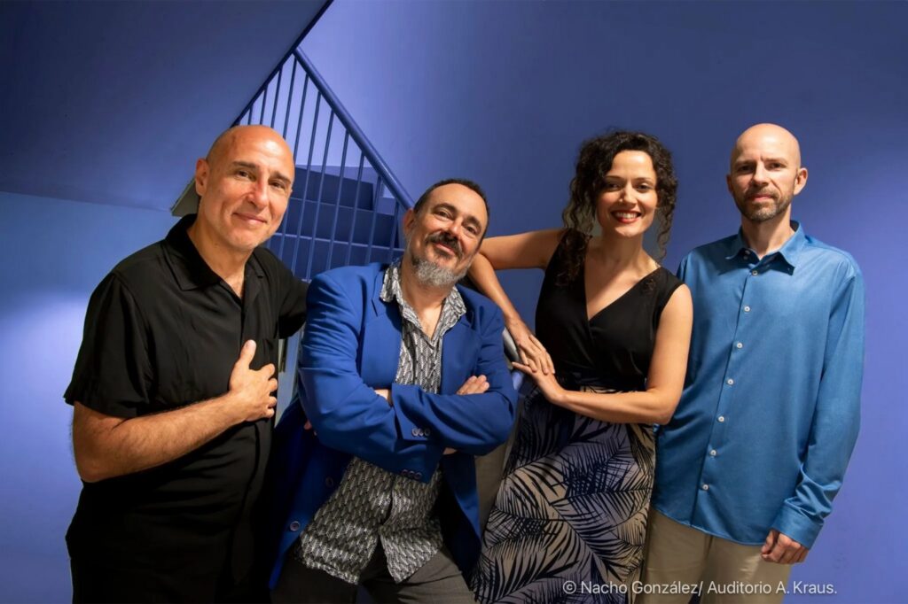 Grupo de cuatro personas sonriendo, fondo azul.