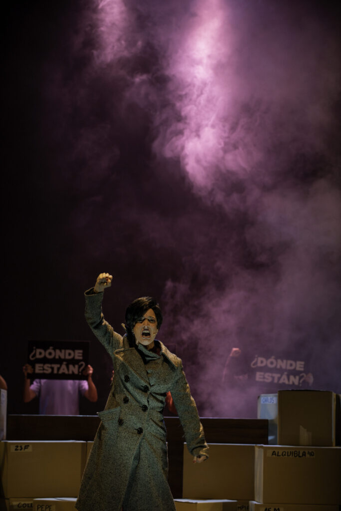Actor en escena con niebla violeta, cajas y carteles.