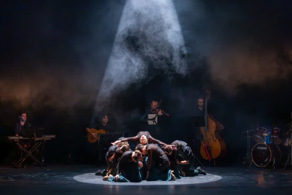 Grupo de bailarines actuando en escenario oscuro