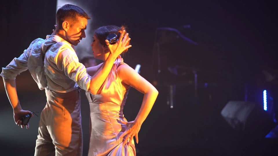 Pareja bailando tango en escenario iluminado.