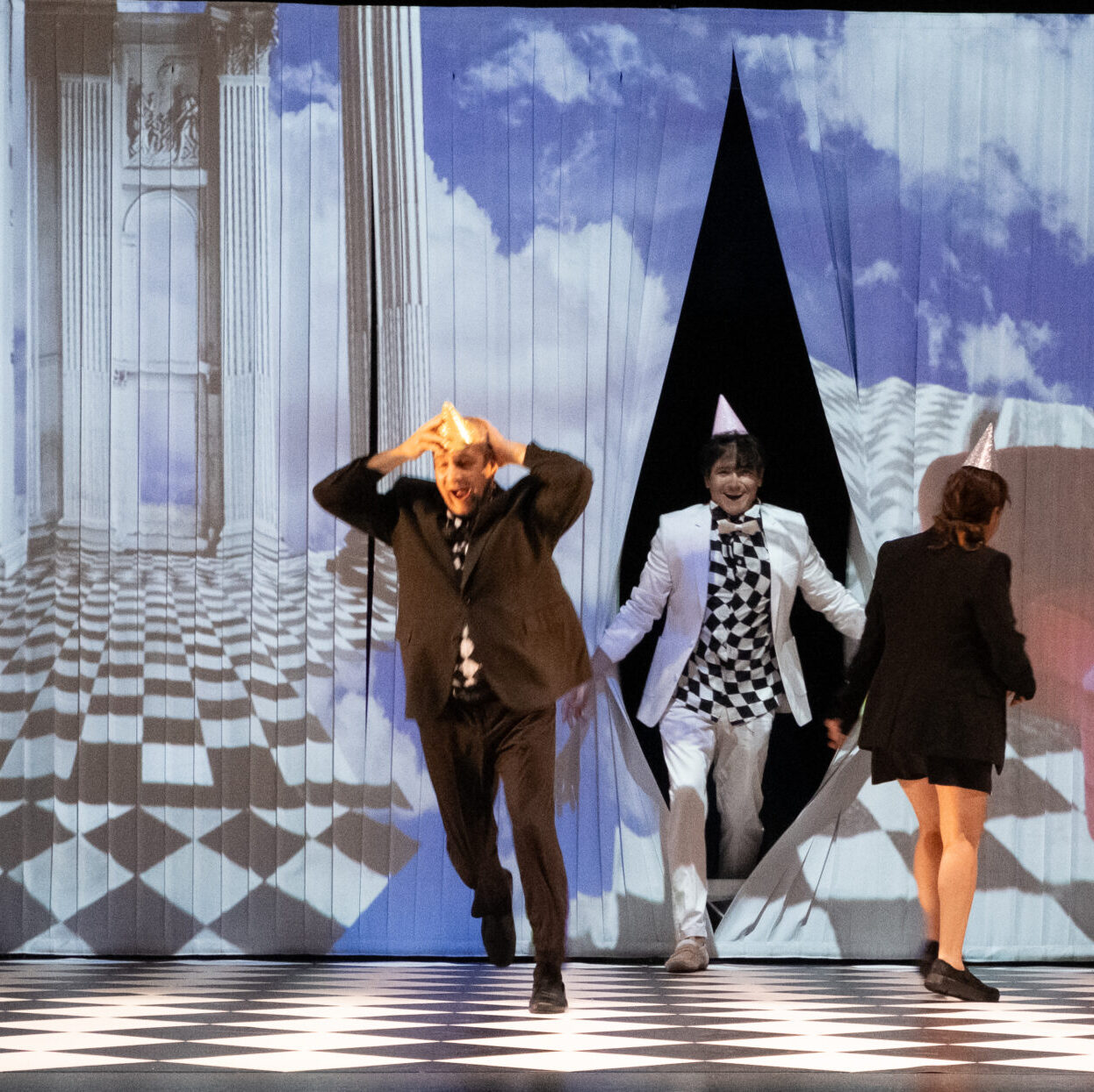 Actores en escenario con fondo surrealista, geometría a cuadros.