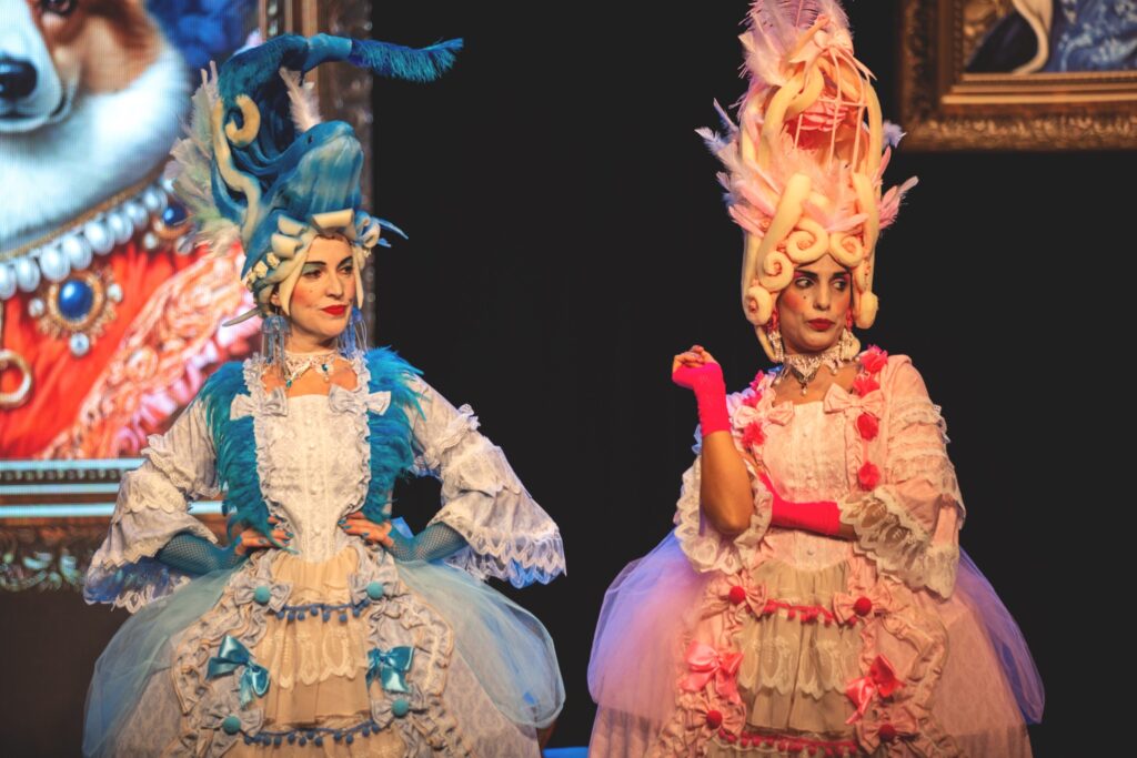 Mujeres con trajes y pelucas extravagantes en escenario.