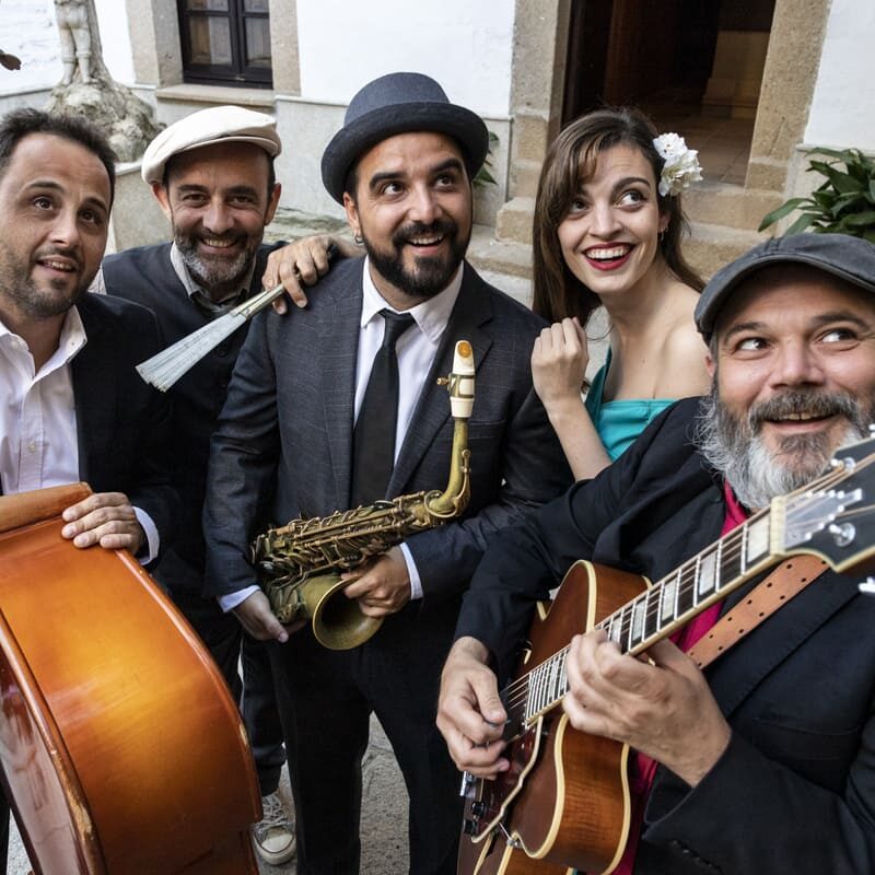 Grupo de músicos sonrientes con instrumentos al aire libre.