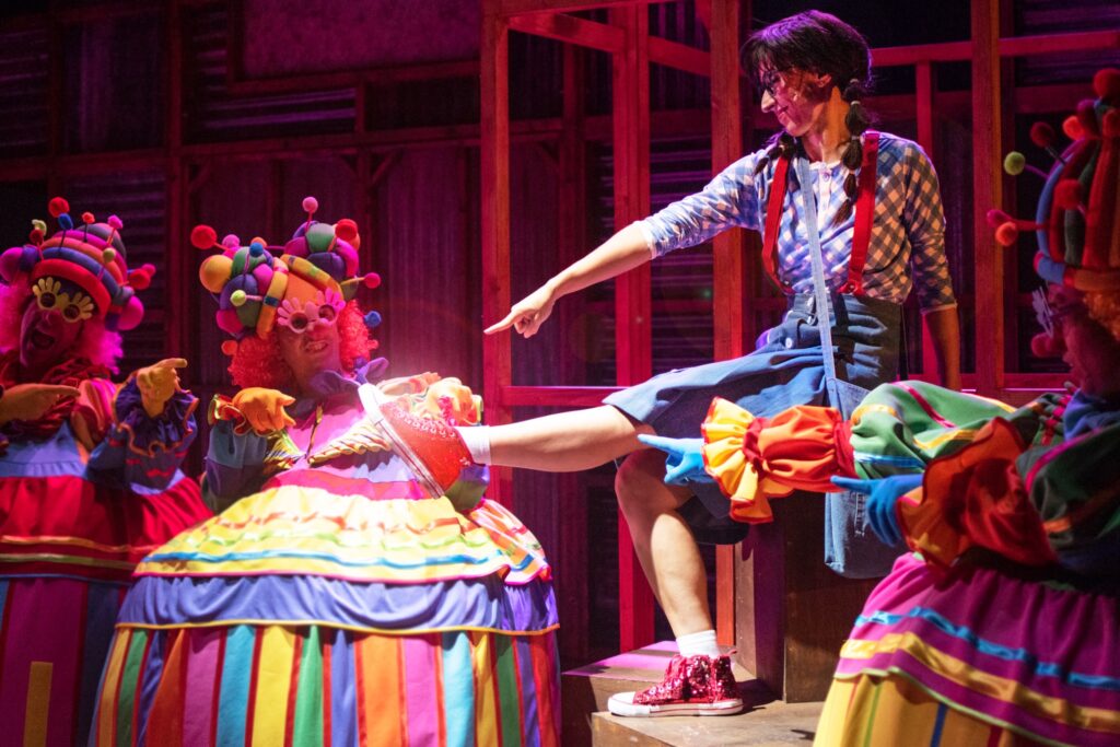 Payasos y persona sonríen en actuación teatral colorida.