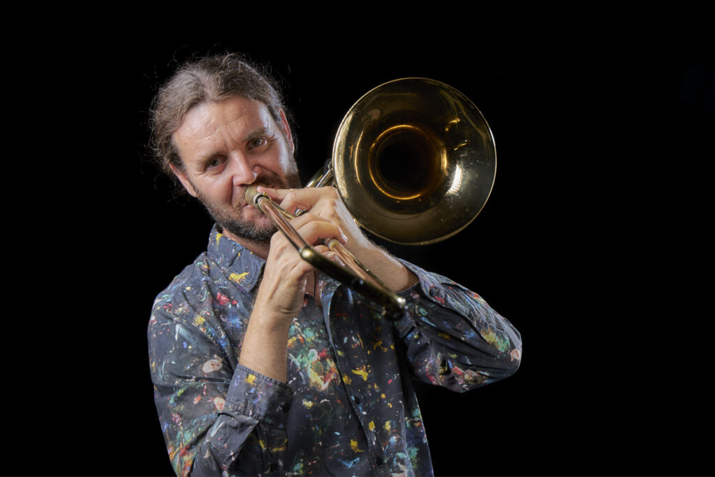 Hombre tocando trombón con camisa estampada colorida.