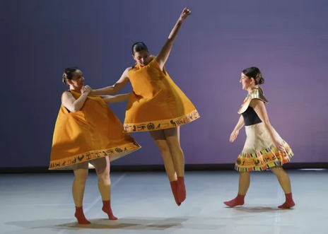 Tres bailarinas con vestidos naranjas en escenario.