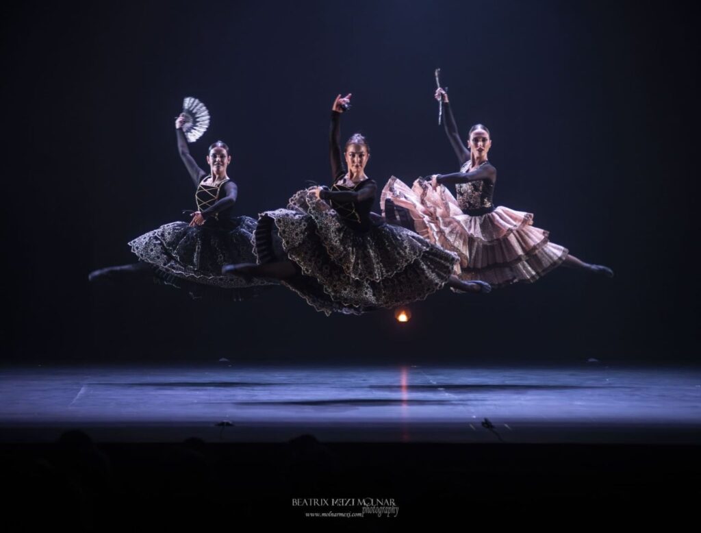 Tres bailarinas realizando salto en escenario oscuro.