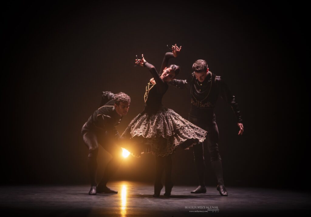 Bailarines actuando en un escenario oscuro, iluminación cálida.