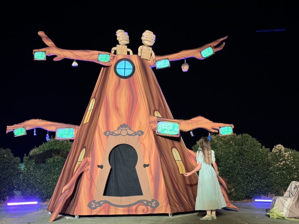 Escena teatral con árbol mágico y actriz.