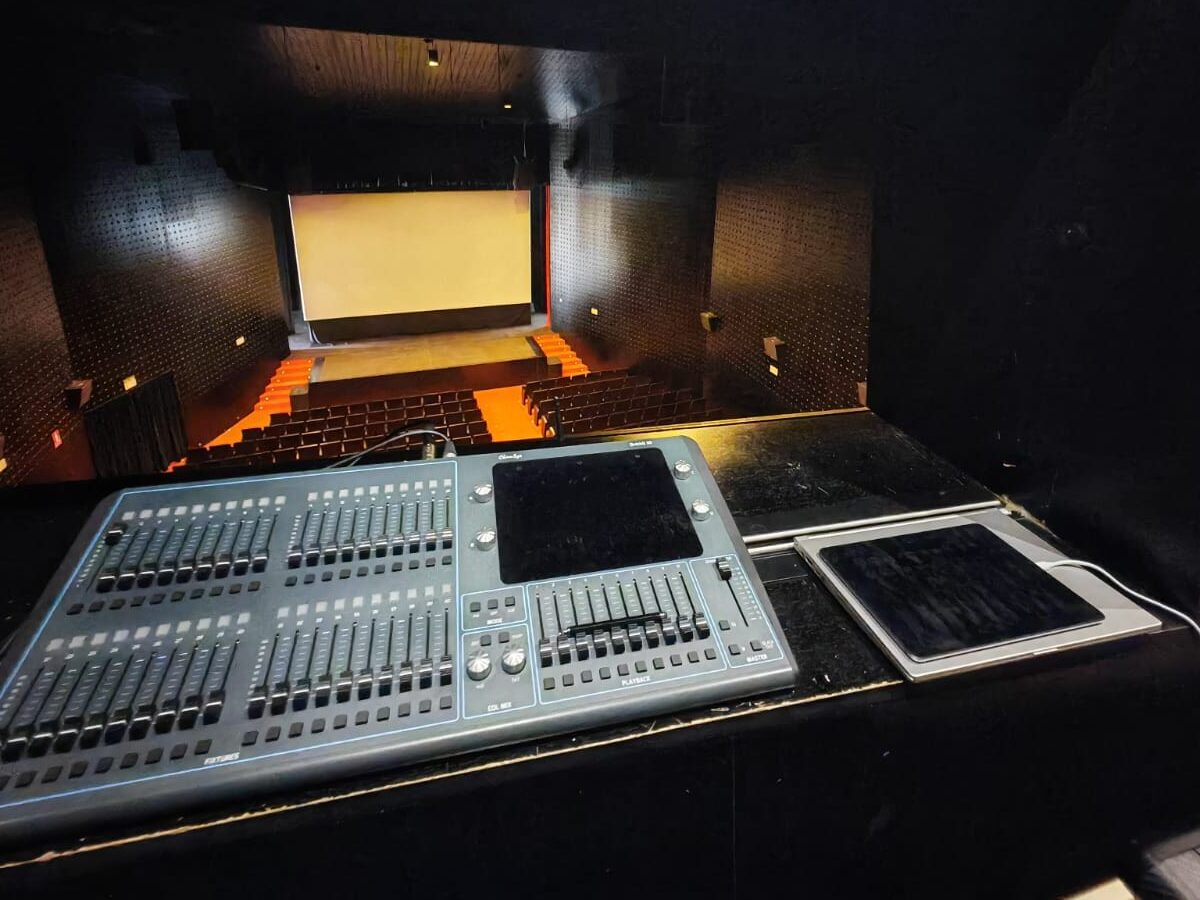 Cabina de control en auditorio con pantalla grande.