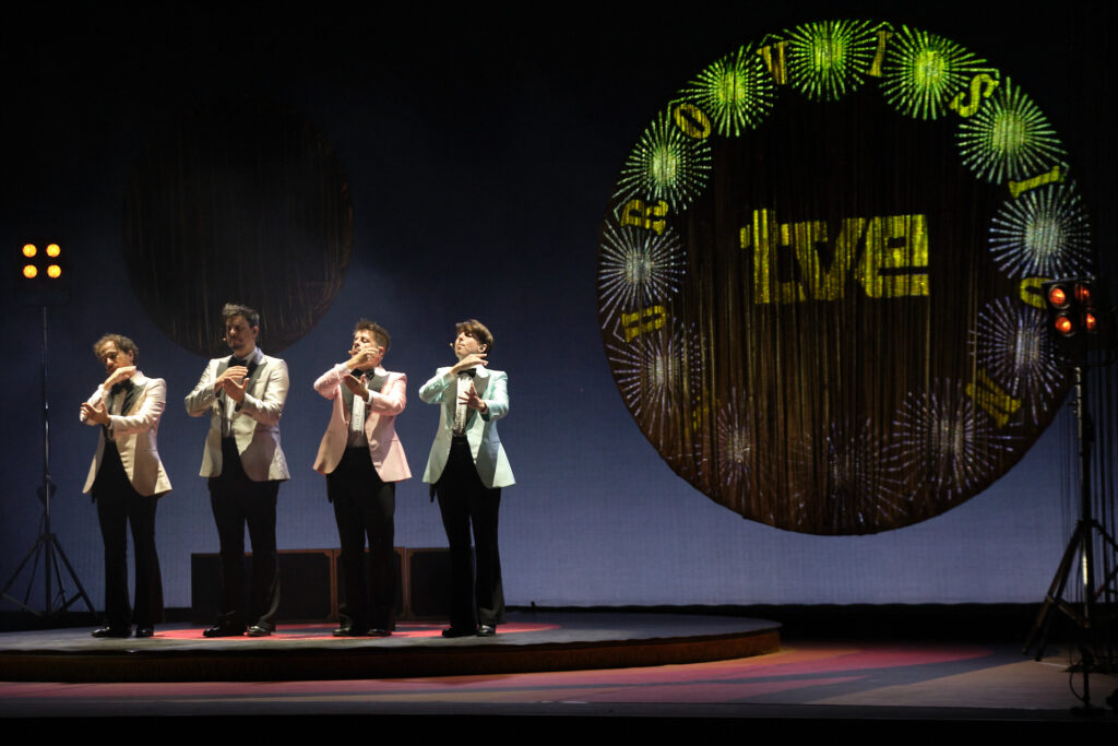 Actuación de cuatro hombres en escenario iluminado.