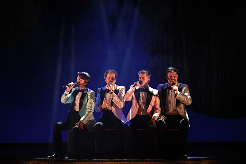 Cuatro cantantes en escenario con micrófonos.