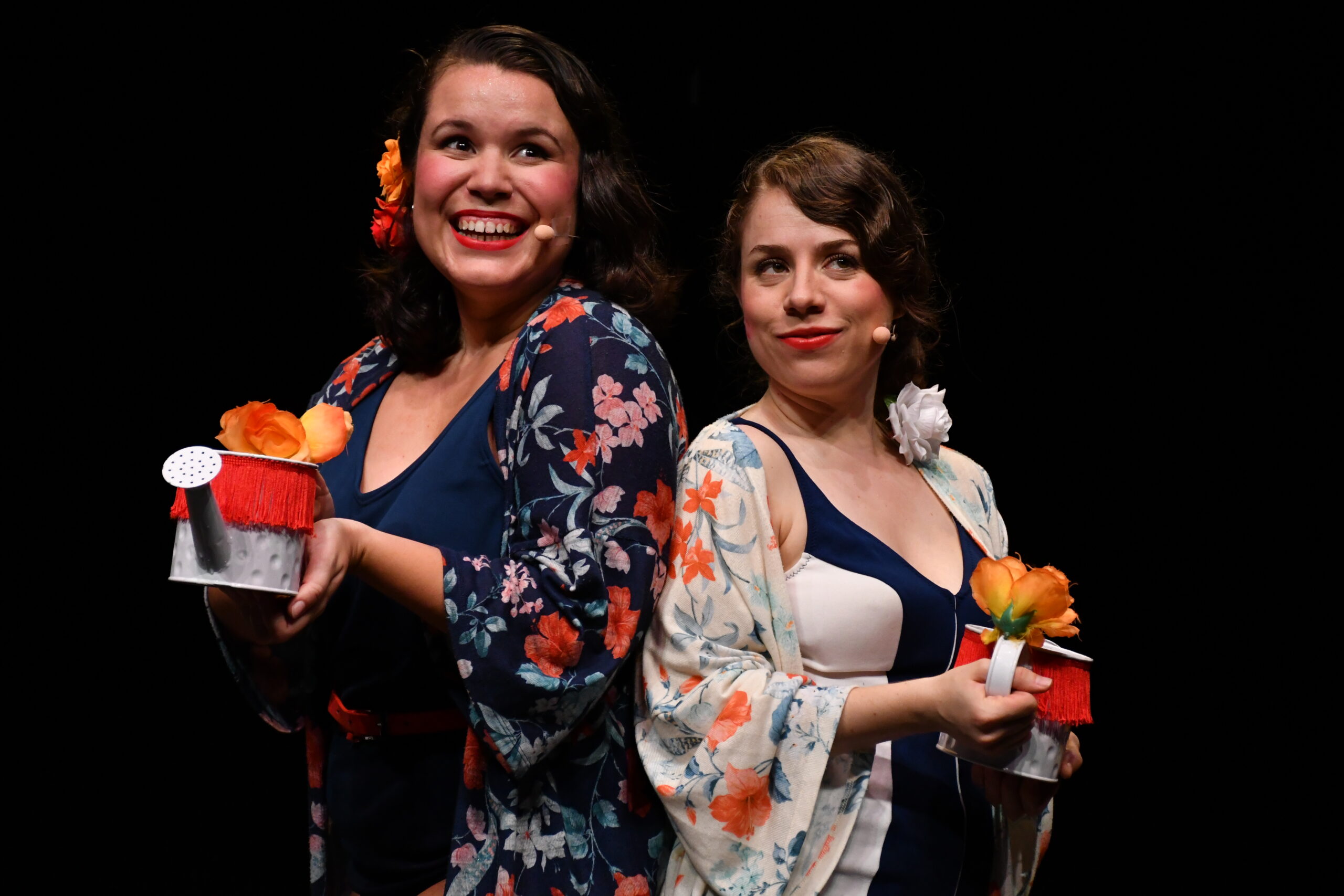 Dos mujeres sonríen con regaderas en mano.