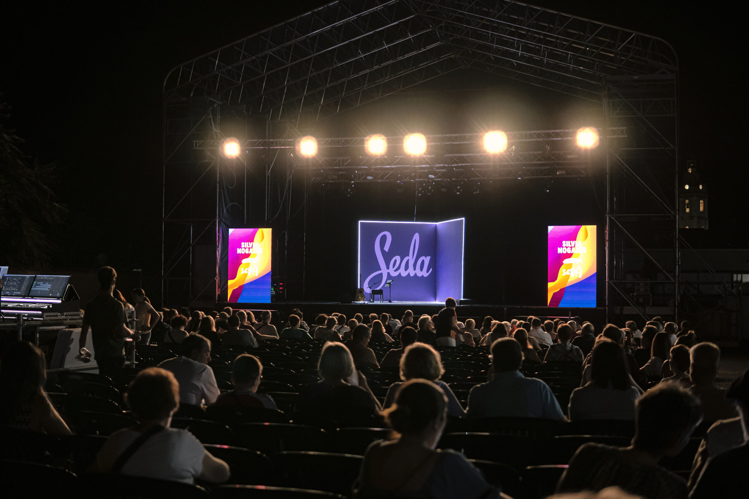 Escenario iluminado frente a público esperando espectáculo nocturno.