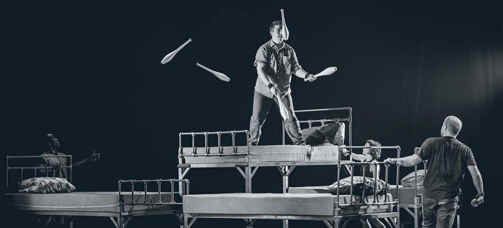 Malabarista actuando sobre camas en escenario teatral.