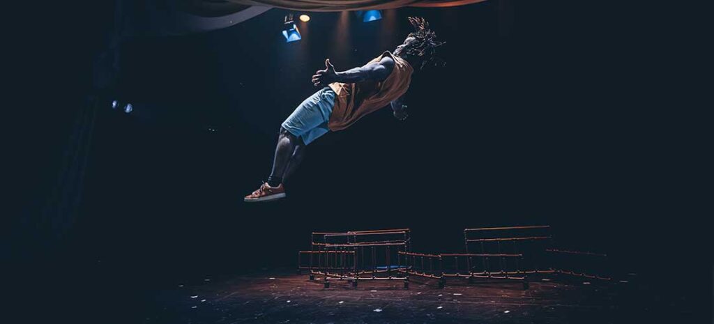 Acróbata realizando salto aéreo en escenario oscuro.