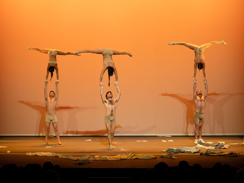 Acrobatas actuando en escenario iluminado, posturas impresionantes.