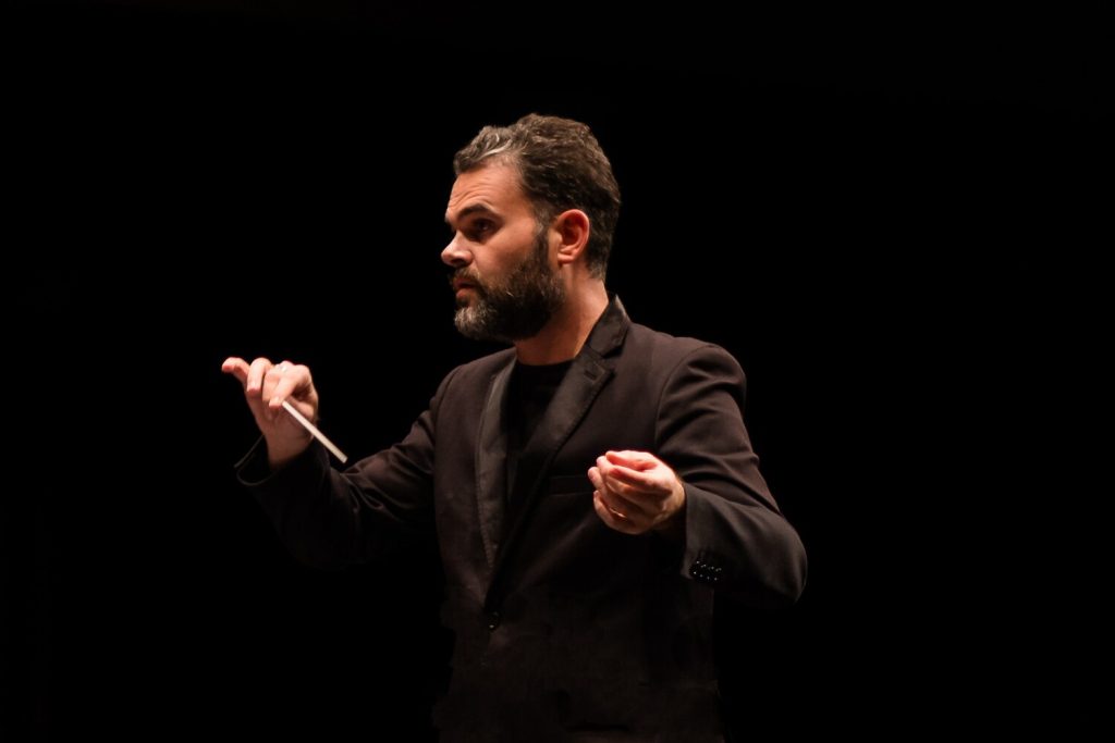 Director de orquesta dirigiendo en escenario oscuro