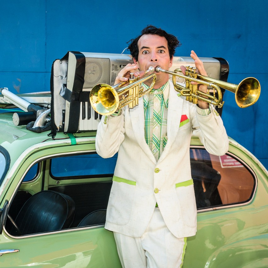 Hombre tocando dos trompetas sobre coche vintage