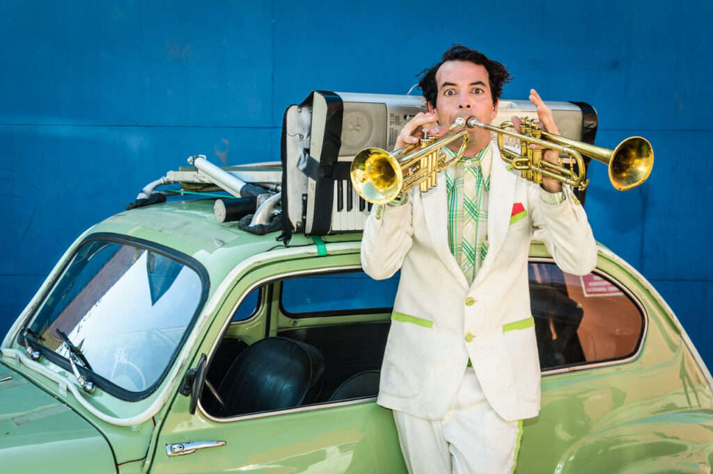 Hombre tocando dos trompetas sobre coche verde