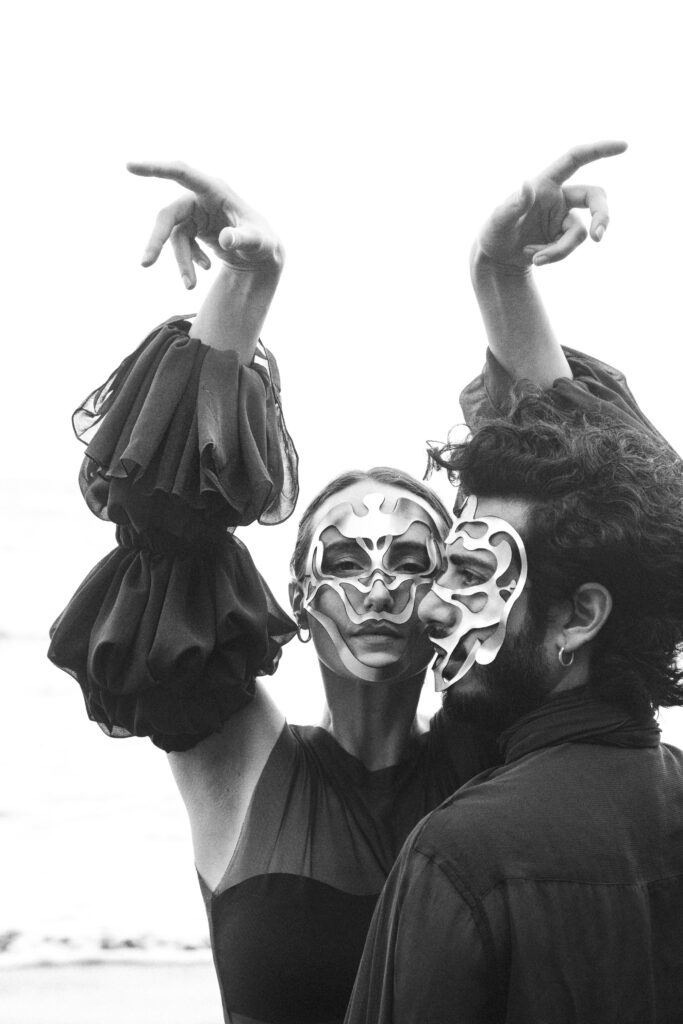 Dos mujeres con máscaras faciales abstractas levantan las manos