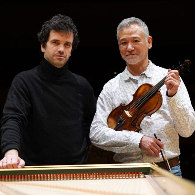 Dos músicos posan con violín junto a un piano