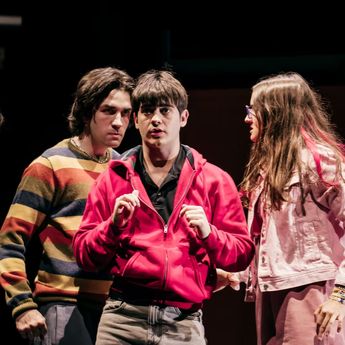 Tres jóvenes interpretan una escena teatral bajo focos
