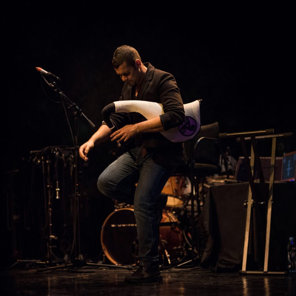 Músico sentado en escenario oscuro junto a un micrófono