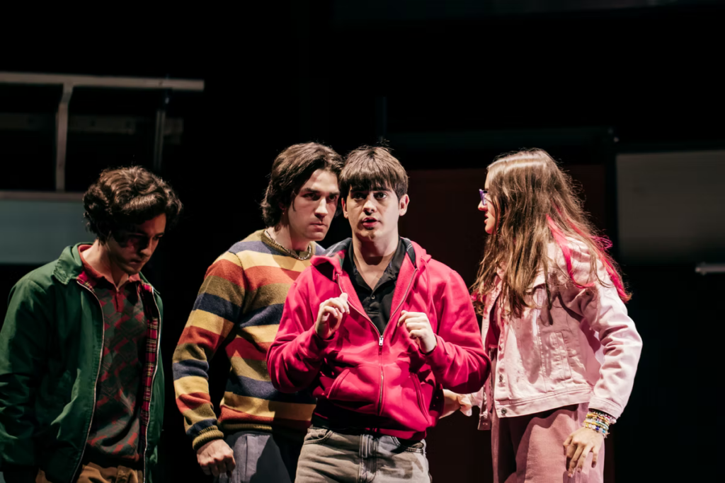 Cuatro jóvenes interpretan una escena teatral bajo focos