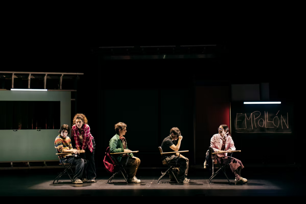 Actores sentados en pupitres durante una obra teatral
