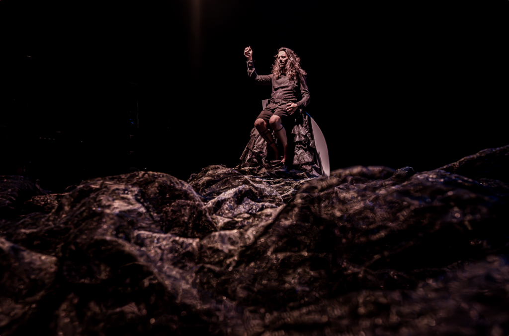 Actor sentado entre rocas bajo un foco teatral