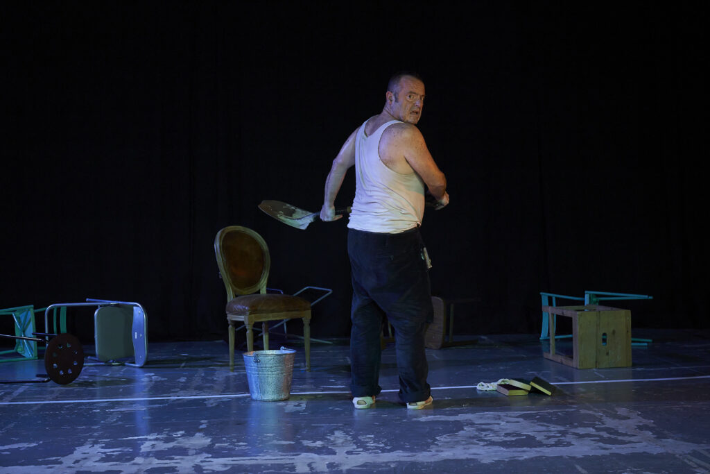 Actor carga una silla en un escenario oscuro